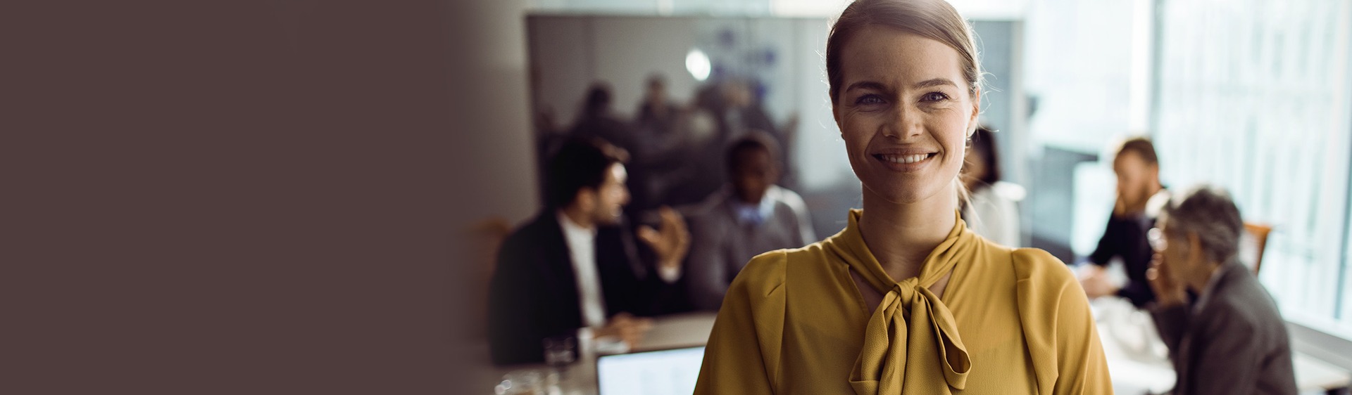 Femme en chemise jaune souriante dans un bureau avec ses collègues en arrière-plan